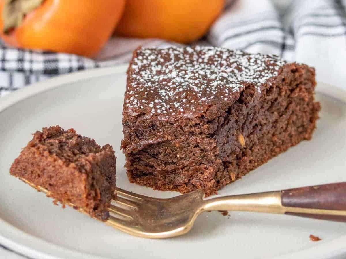 Slice of chocolate persimmon cake with bites taken and a piece on a fork.