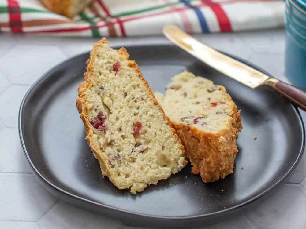 sliced cranberry soda bread on a black plate with loaf behind