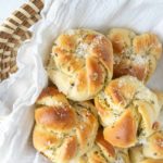 A basket of freshly baked garlic knots topped with grated cheese, resting on a white cloth.