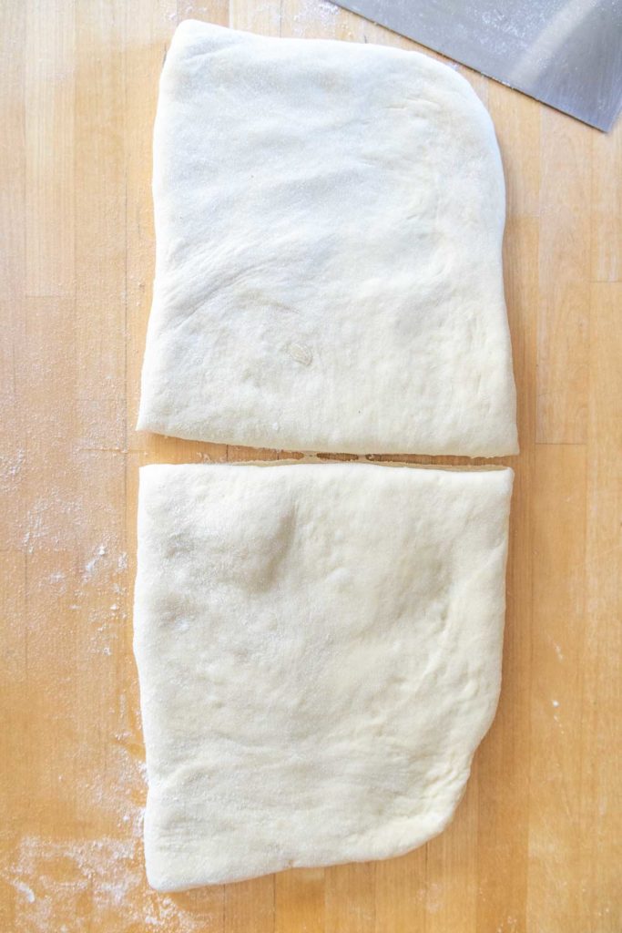 Two pieces of rectangular pizza dough on a floured wooden surface.