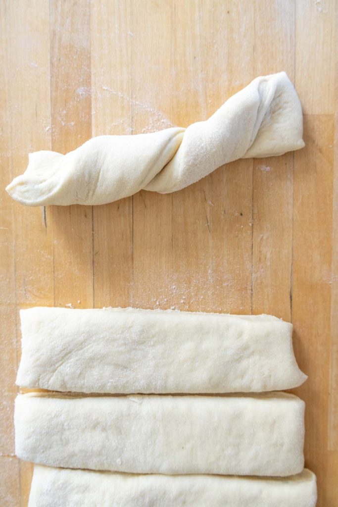 Bread dough on a wooden surface with one piece twisted and three pieces lying flat.