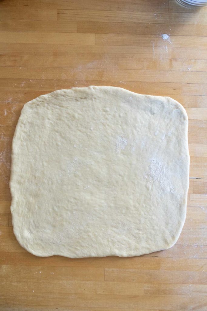 A rectangle of rolled-out dough on a wooden surface, dusted with flour.