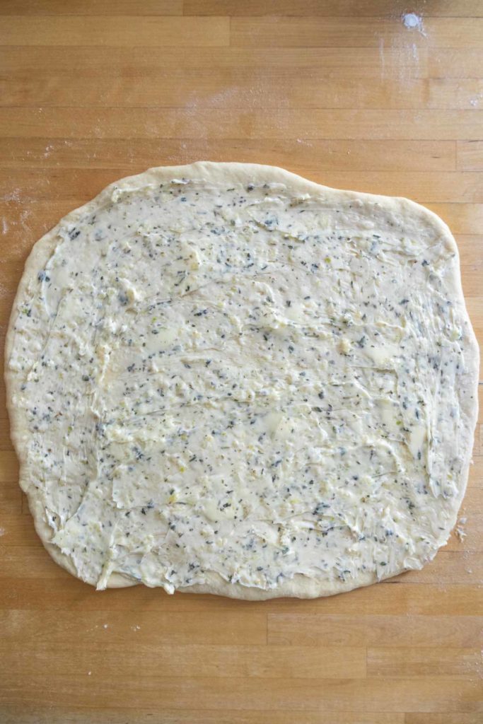 Rolled-out dough with flecks of herbs on a wooden surface.