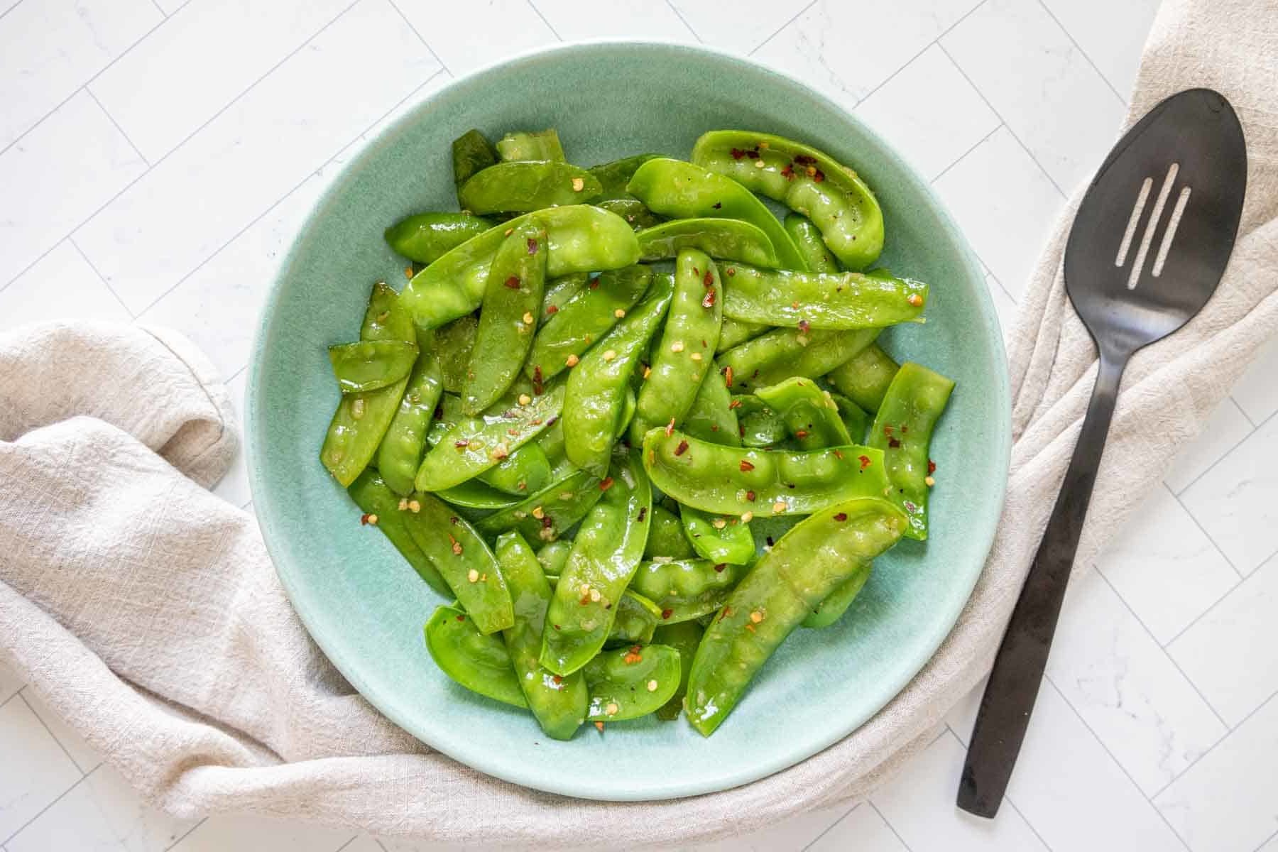 Overhead of sautéed snow peas on a blue plate.