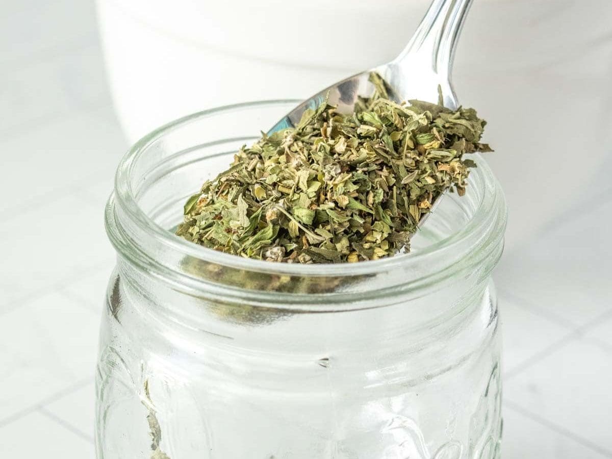 A spoonful of herbs in a glass jar.