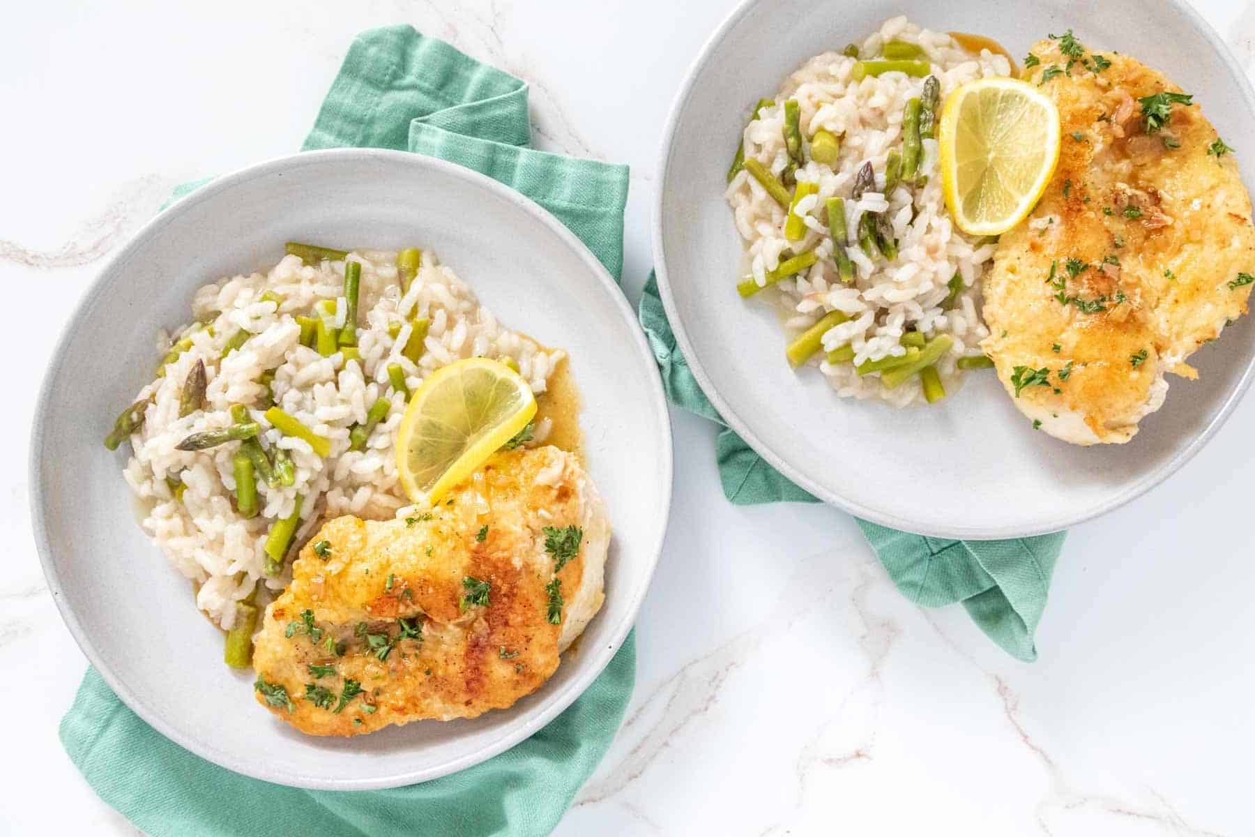 Overhead of lemon chicken and asparagus risotto on plates.