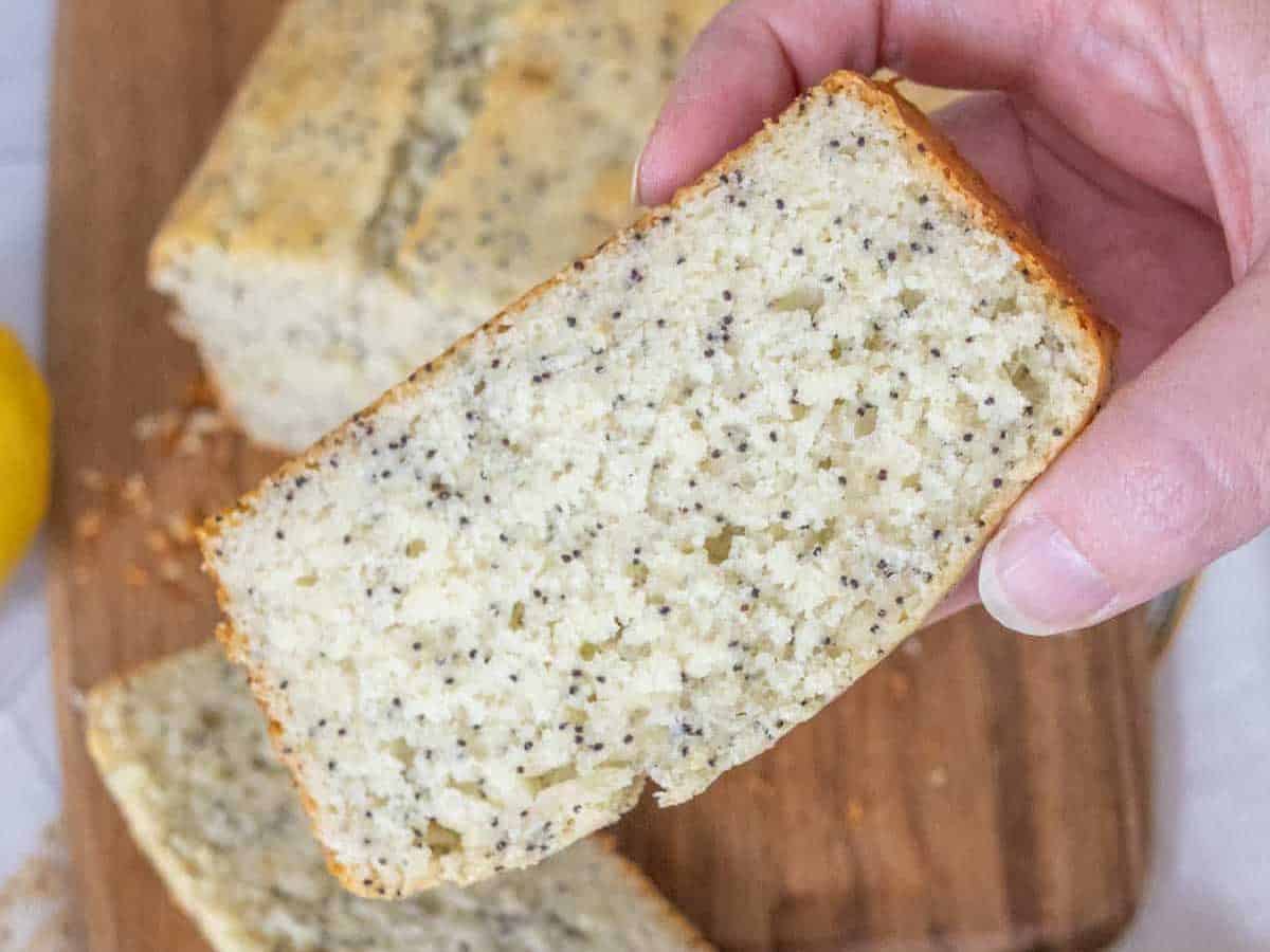 Hand holding up a slice of lemon poppy seed bread.