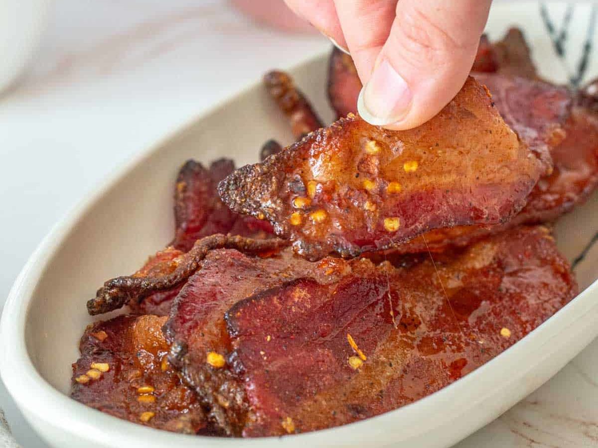 fingers picking up candied bacon slice