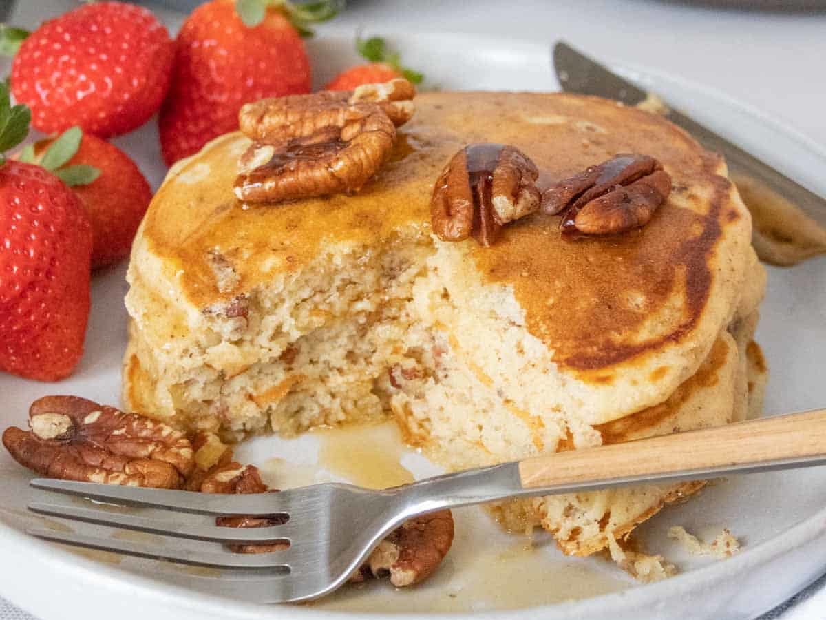 Pecan pancakes on a plate with a few pieces cut out and a fork in front.