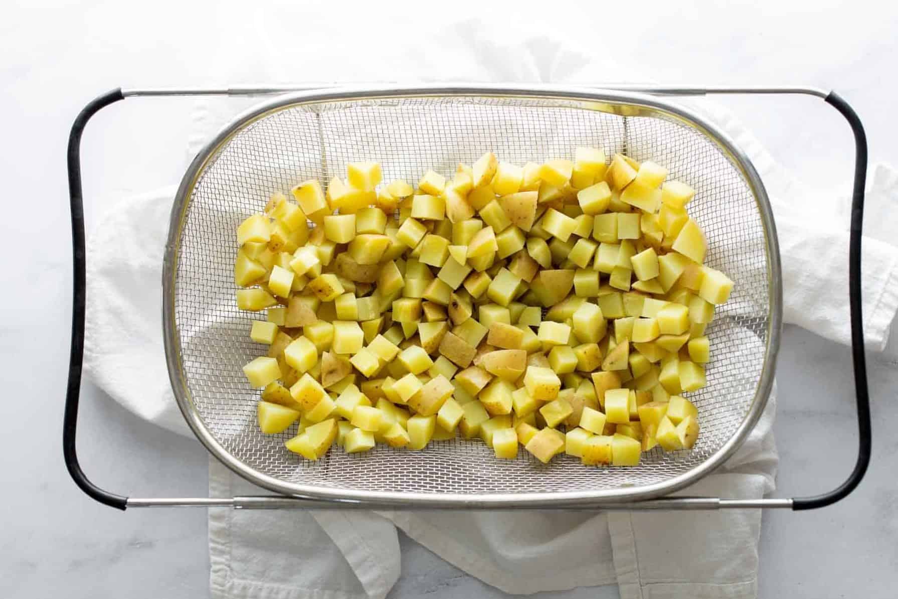 Diced potatoes on a mesh strainer over a white surface.