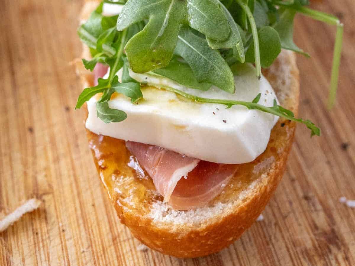 A sandwich with ham, cheese and arugula on a wooden cutting board.