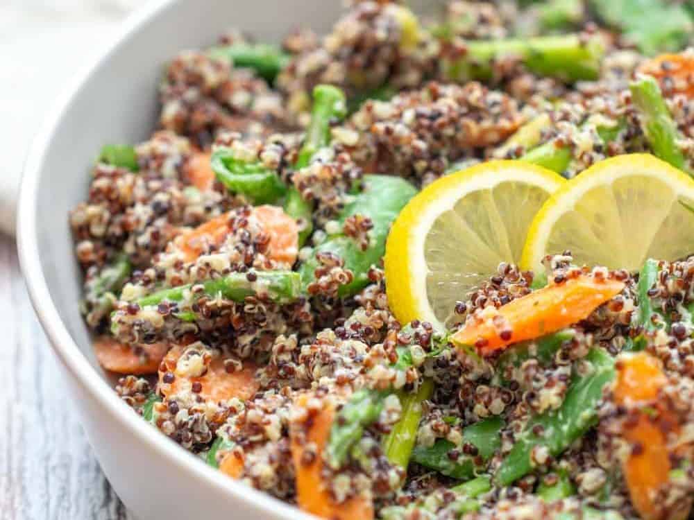 gray serving dish of quinoa primavera with lemon slices on top