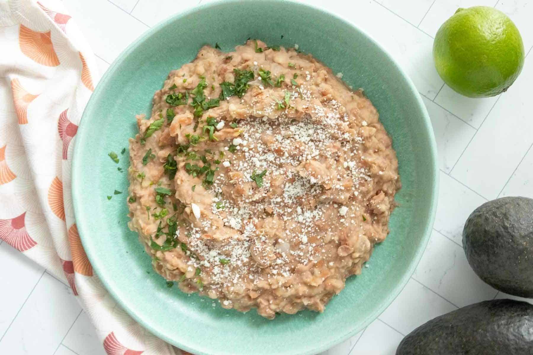 A bowl of refried beans on a table next to a lime.