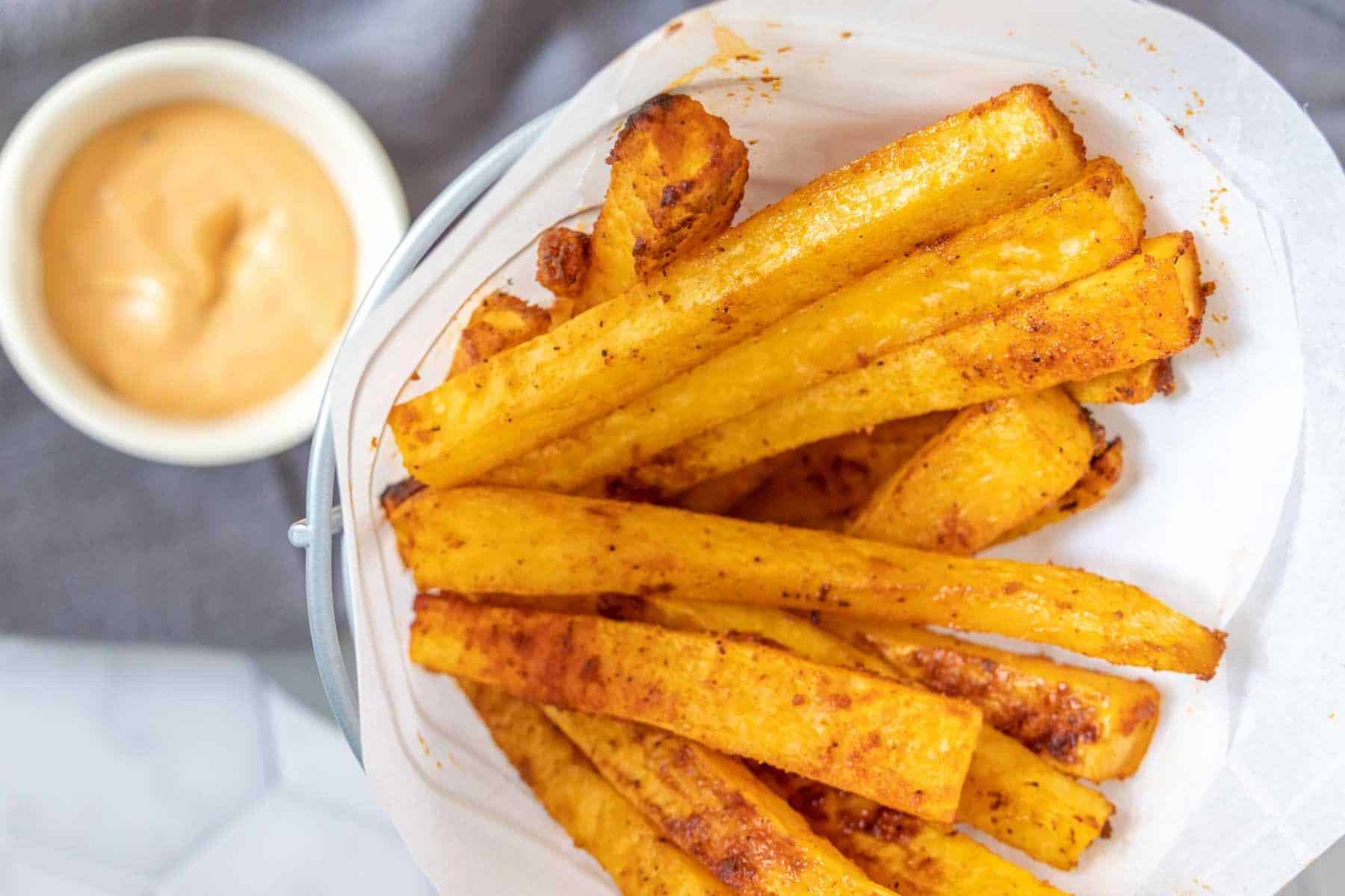 Overhead of rutabaga fries in a fry basket with burger sauce.