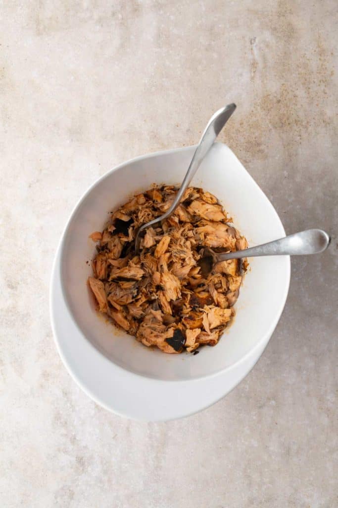 Bowl of shredded tuna with two metal forks on a textured surface.