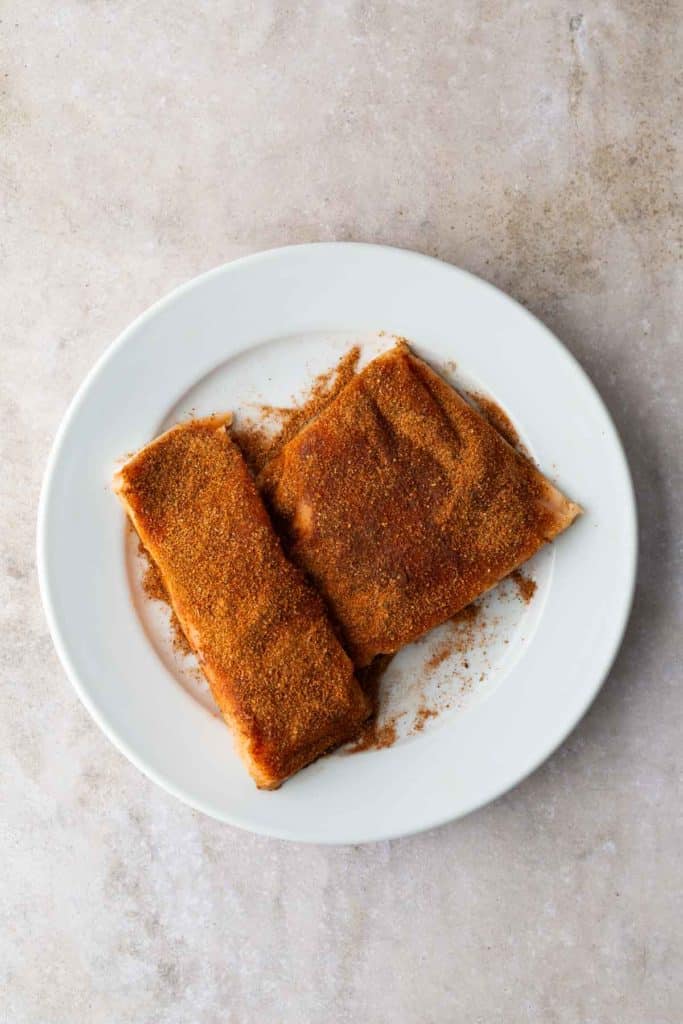 Two slices of toast on a white plate, each topped with a layer of cinnamon and sugar.