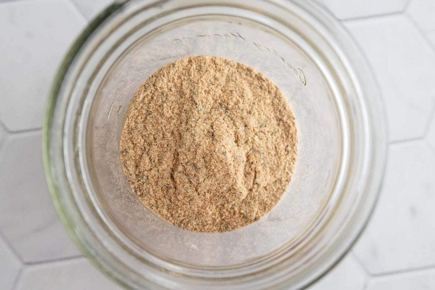 A glass jar filled with light brown powder on a hexagonal tiled surface.