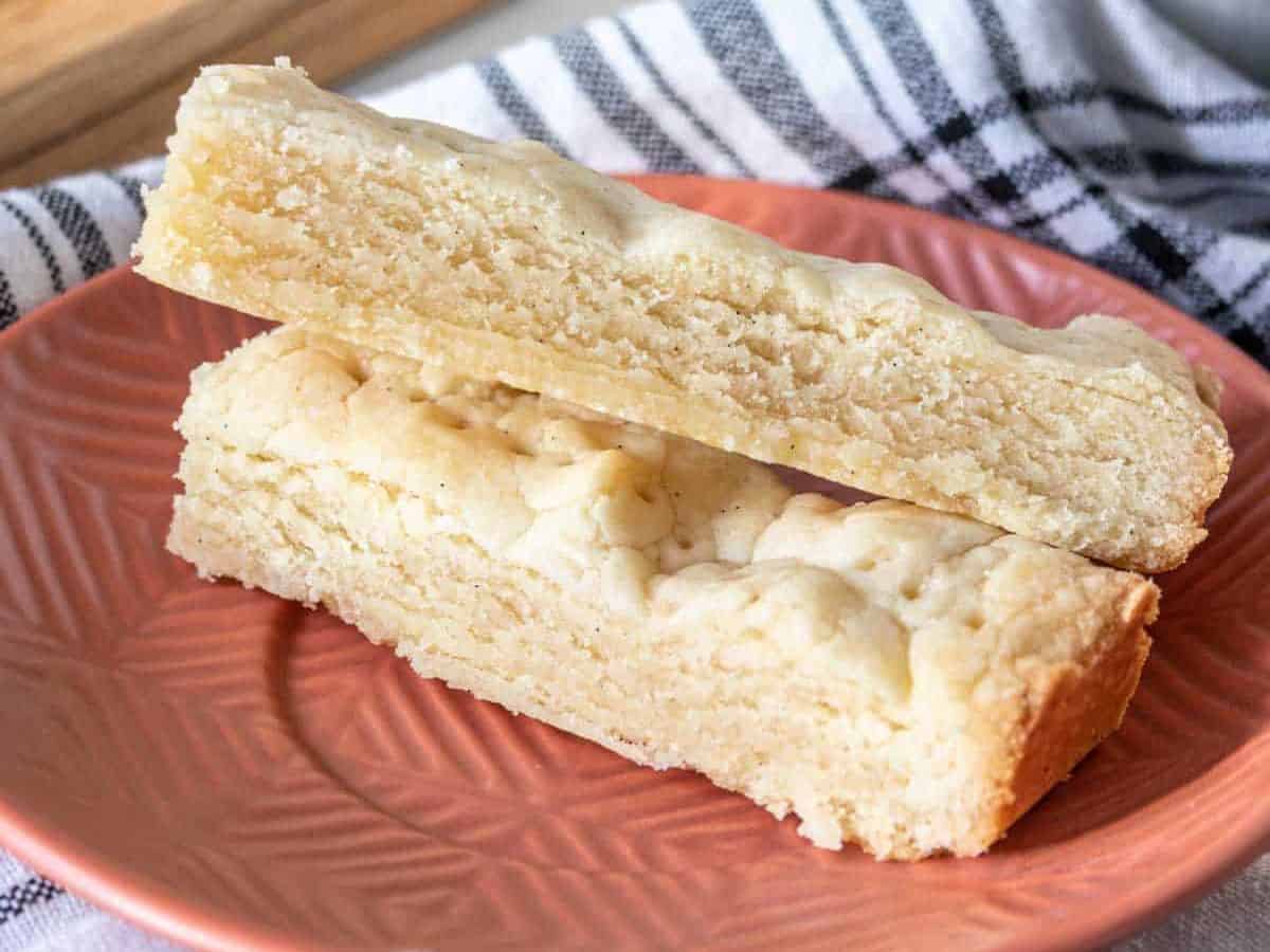 Two pieces of shortbread stacked on an orange plate showing the cookie texture.