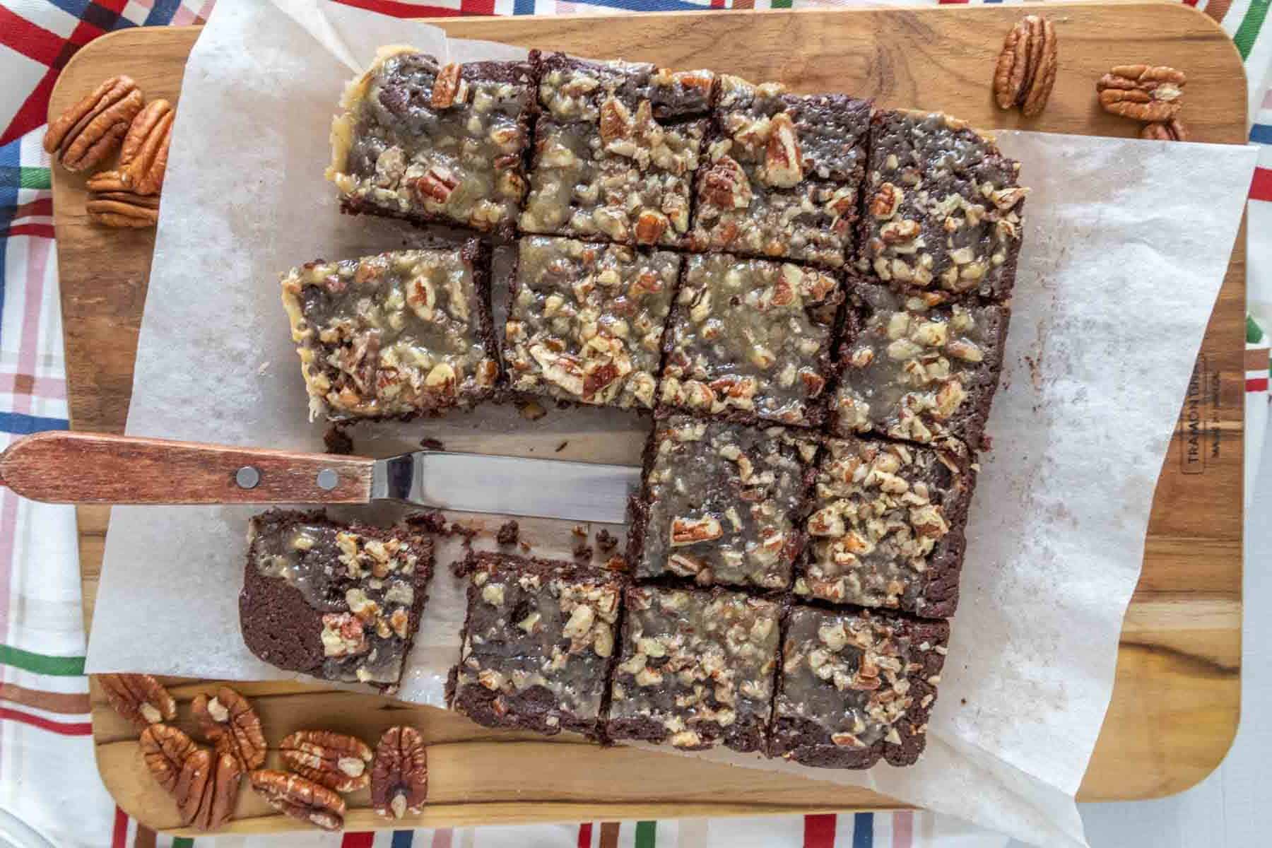 Overhead of a cut batch of turtle brownies with pecans and an offset spatula.