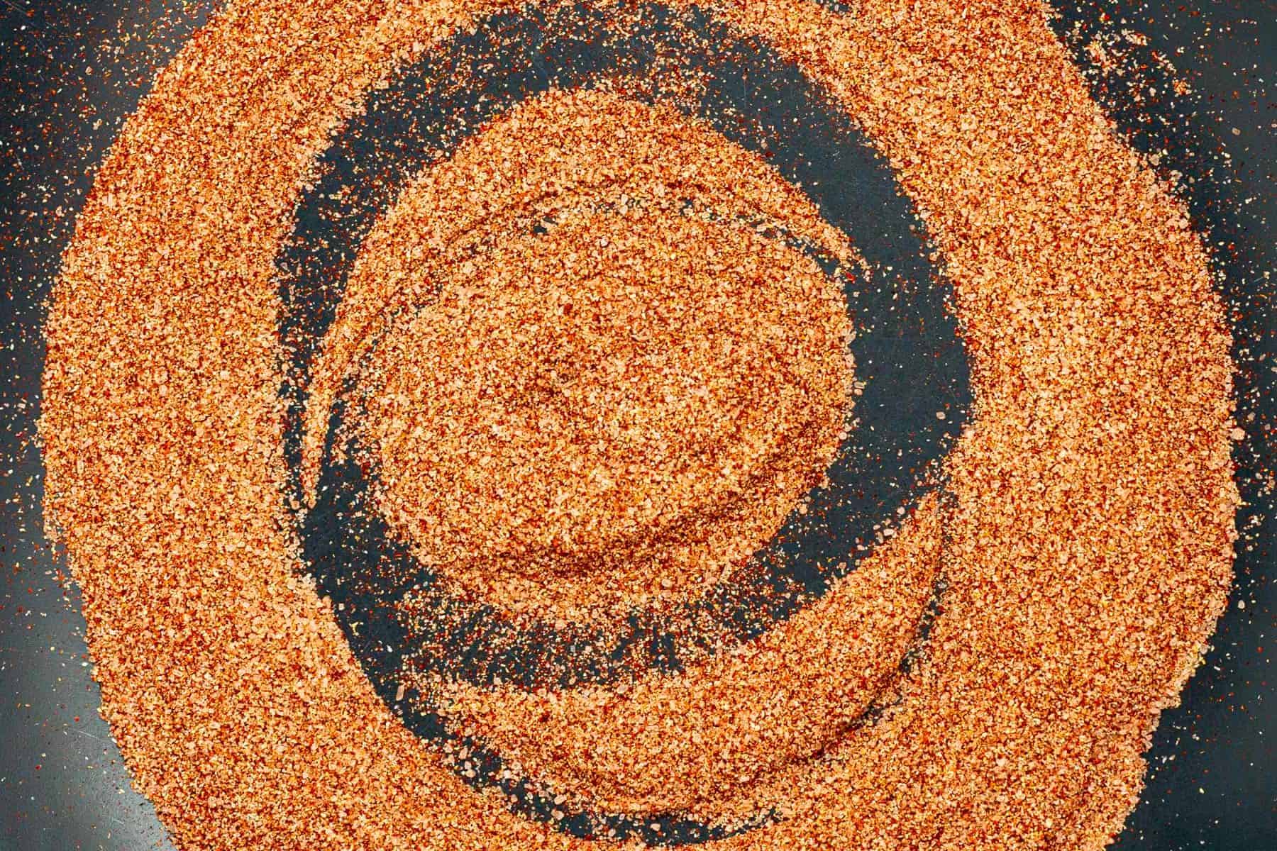 Close-up of granulated seasoning scattered in circular patterns on a dark surface.