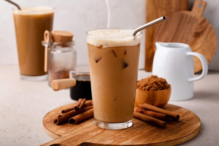 A shaken espresso in a glass with ice and a metal straw sitting on a cutting board.