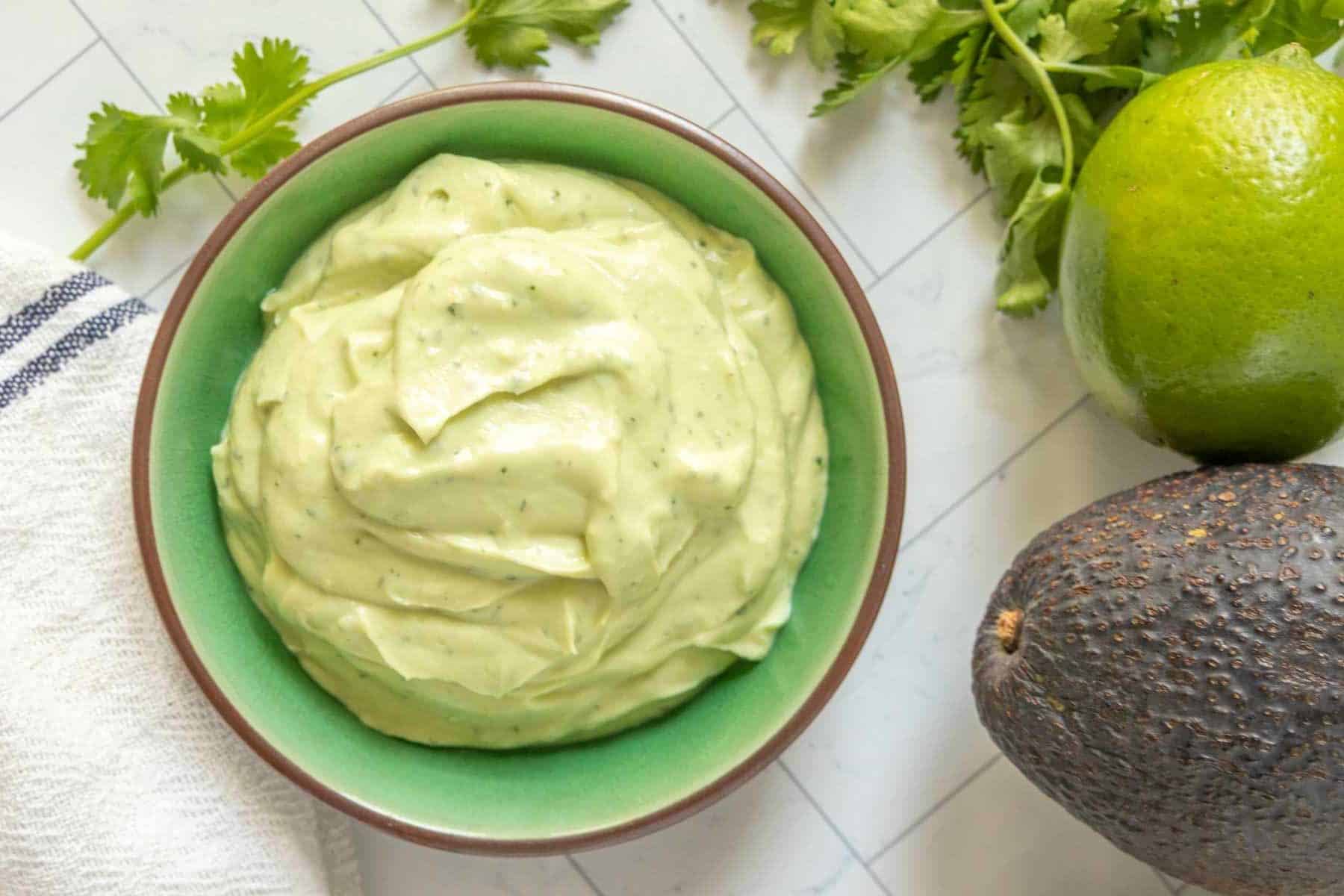 Avocado lime crema in a bowl next to a lime and avocado.