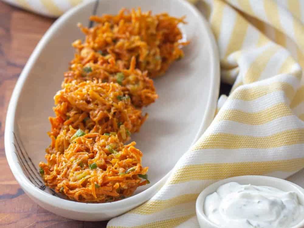 Carrot fritters on a white plate with a yellow napkin and a white bowl of dill sauce.