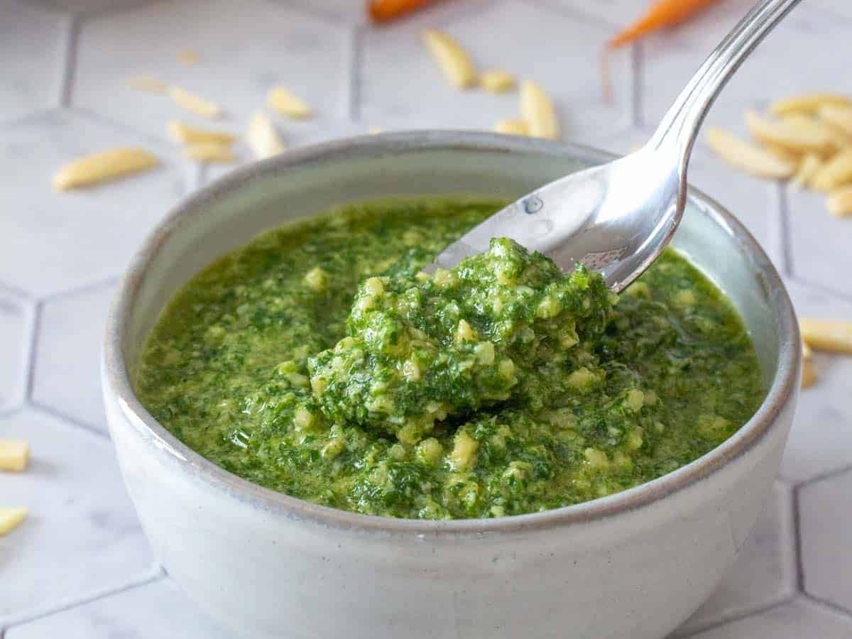 A bowl of carrot top pesto with spoon.