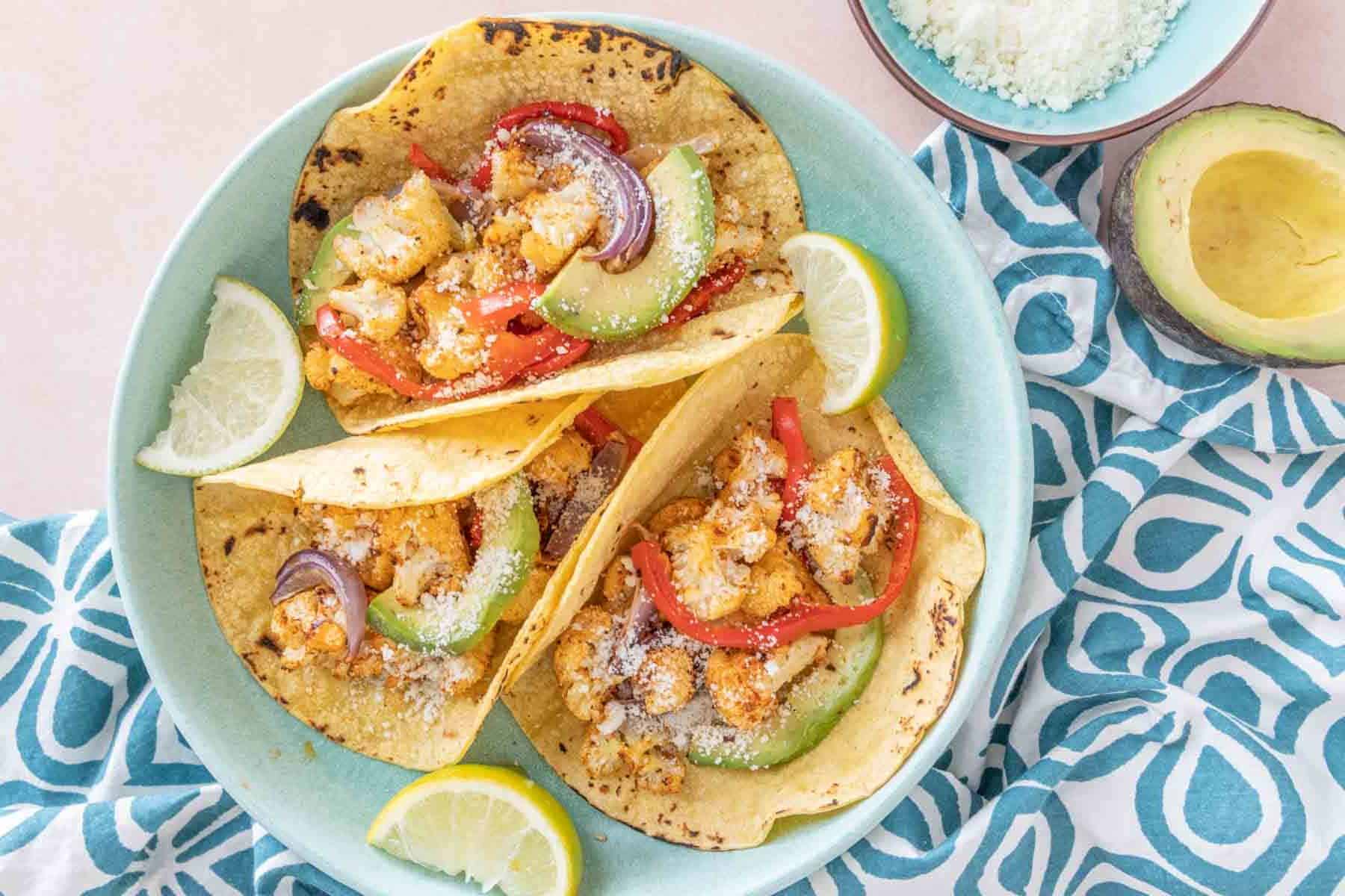 Overhead of three cauliflower tacos on a blue plate with a blue patterned napkin.