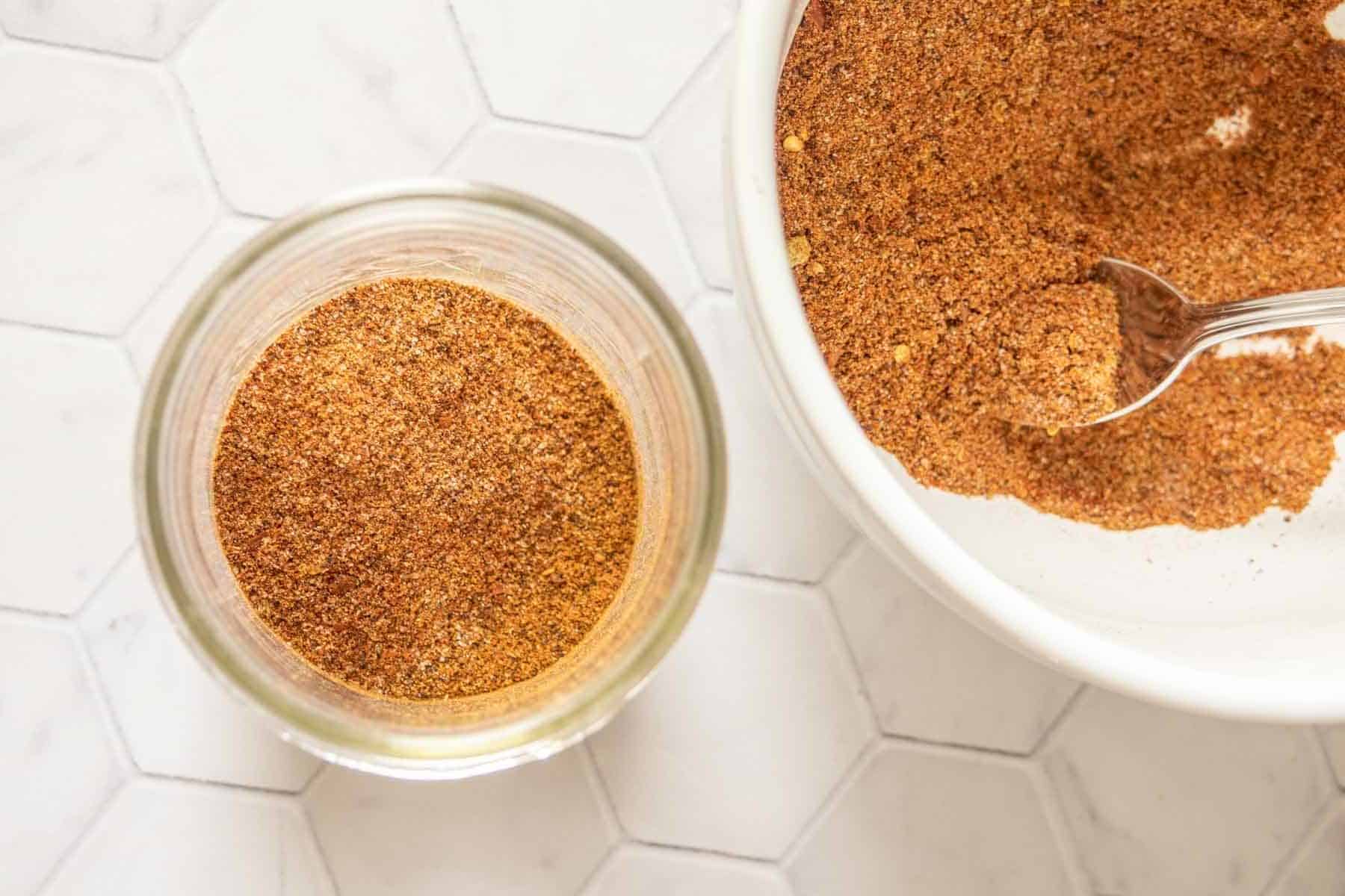 Taco seasoning in a jar next to a bowl of more seasoning.