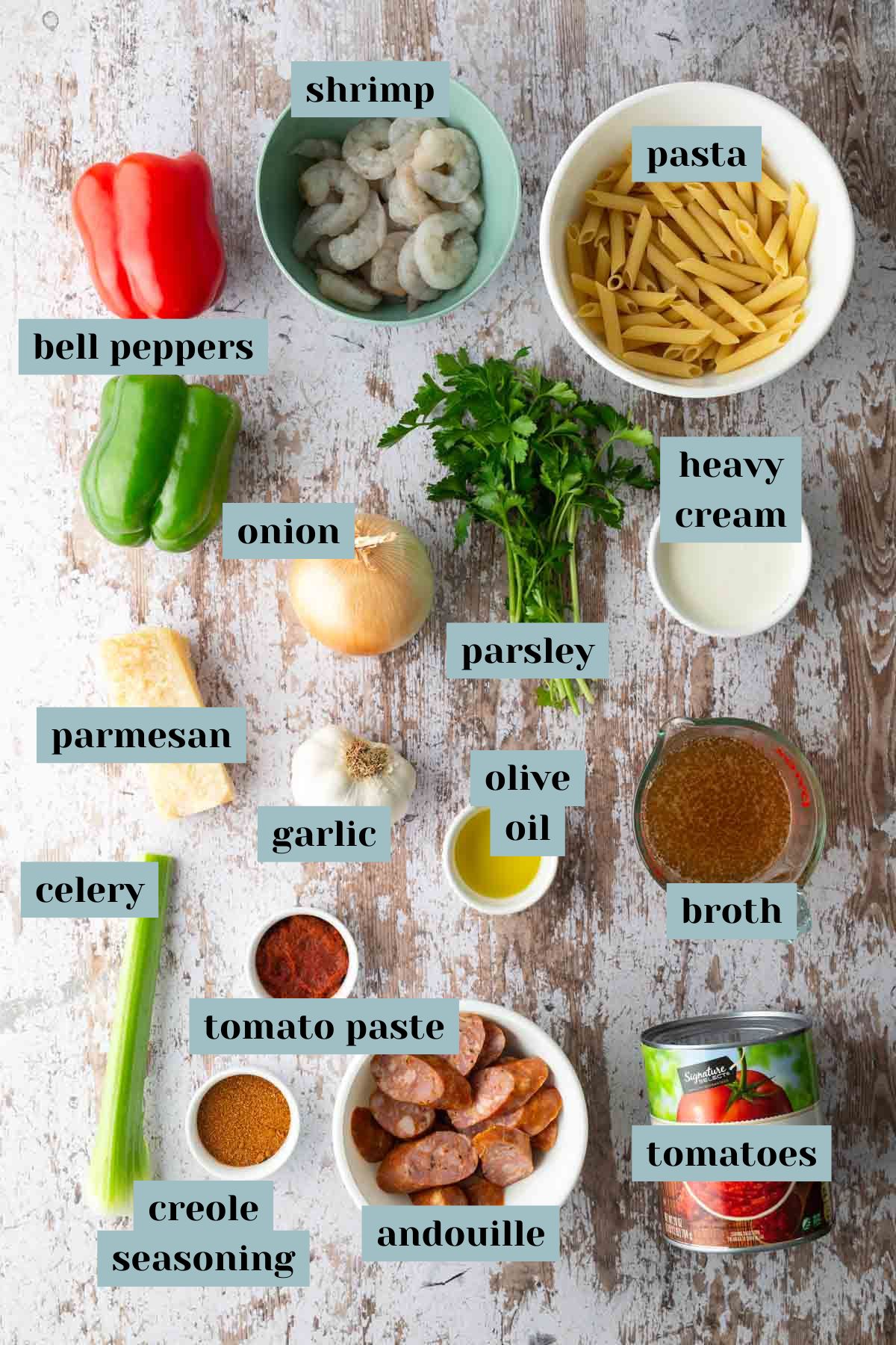 Top-down view of labeled ingredients for a dish, including shrimp, pasta, bell peppers, onion, celery, seasonings, cream, broth, sausage, garlic, olive oil, parsley, tomatoes, and cheese.