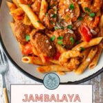 A plate of jambalaya pasta with sausage, bell peppers, and herbs, served on a white dish with a fork on the side.