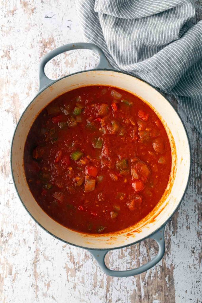 A pot filled with chunky tomato-based sauce with visible pieces of vegetables, placed on a rustic wooden surface, next to a striped cloth.