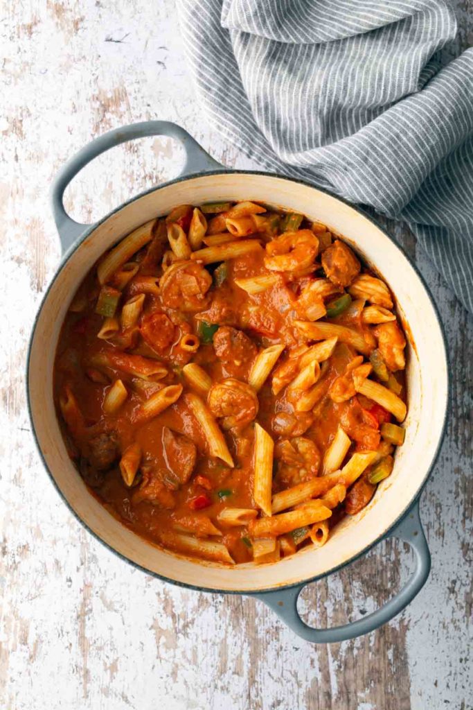 A pot of penne pasta with shrimp, sausage, and vegetables in tomato sauce.