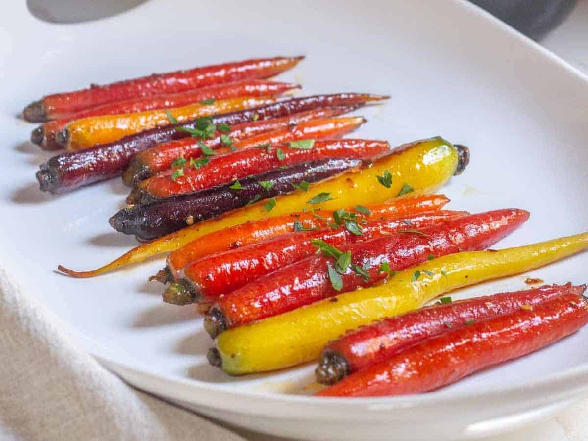 glazed carrots on a serving plate with hand sprinkling parsley