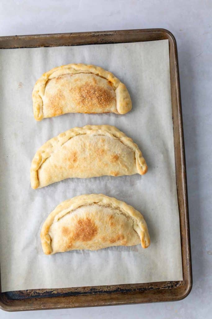 Three baked empanadas on a parchment-lined baking sheet.