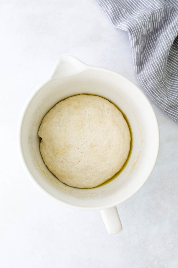 Bowl with risen dough on a light surface, next to a striped cloth.