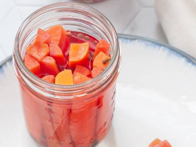 pickled carrots in a jar with carrots and tongs on a plate