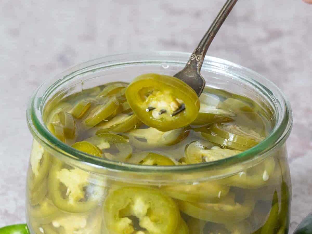 fork holding pickled jalapeño over jar