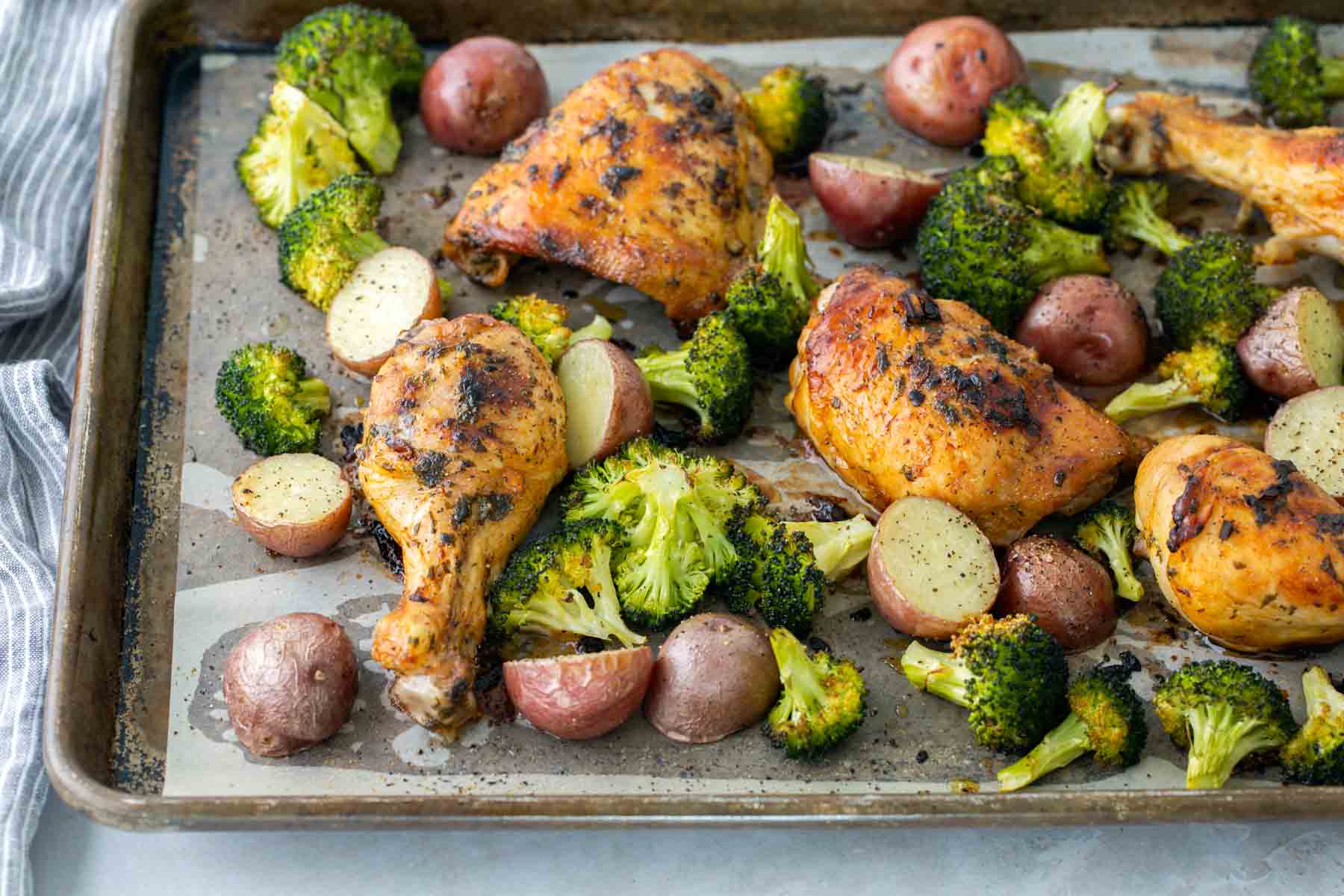 A baking sheet with roasted chicken drumsticks and thighs, red potatoes, and broccoli florets.