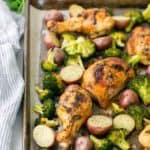 Sheet pan with roasted chicken drumsticks, broccoli, and red potatoes. Striped napkin and lime wedges nearby.