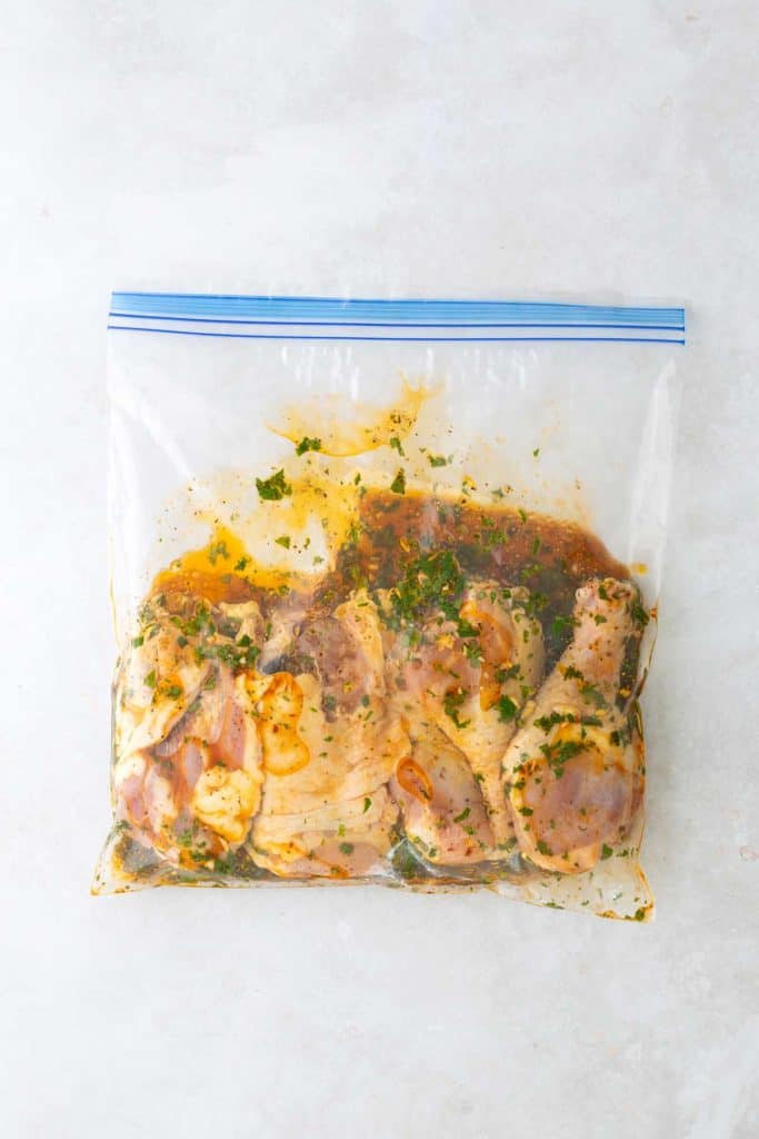 Raw chicken marinating in a plastic zipper bag with herbs and sauce.