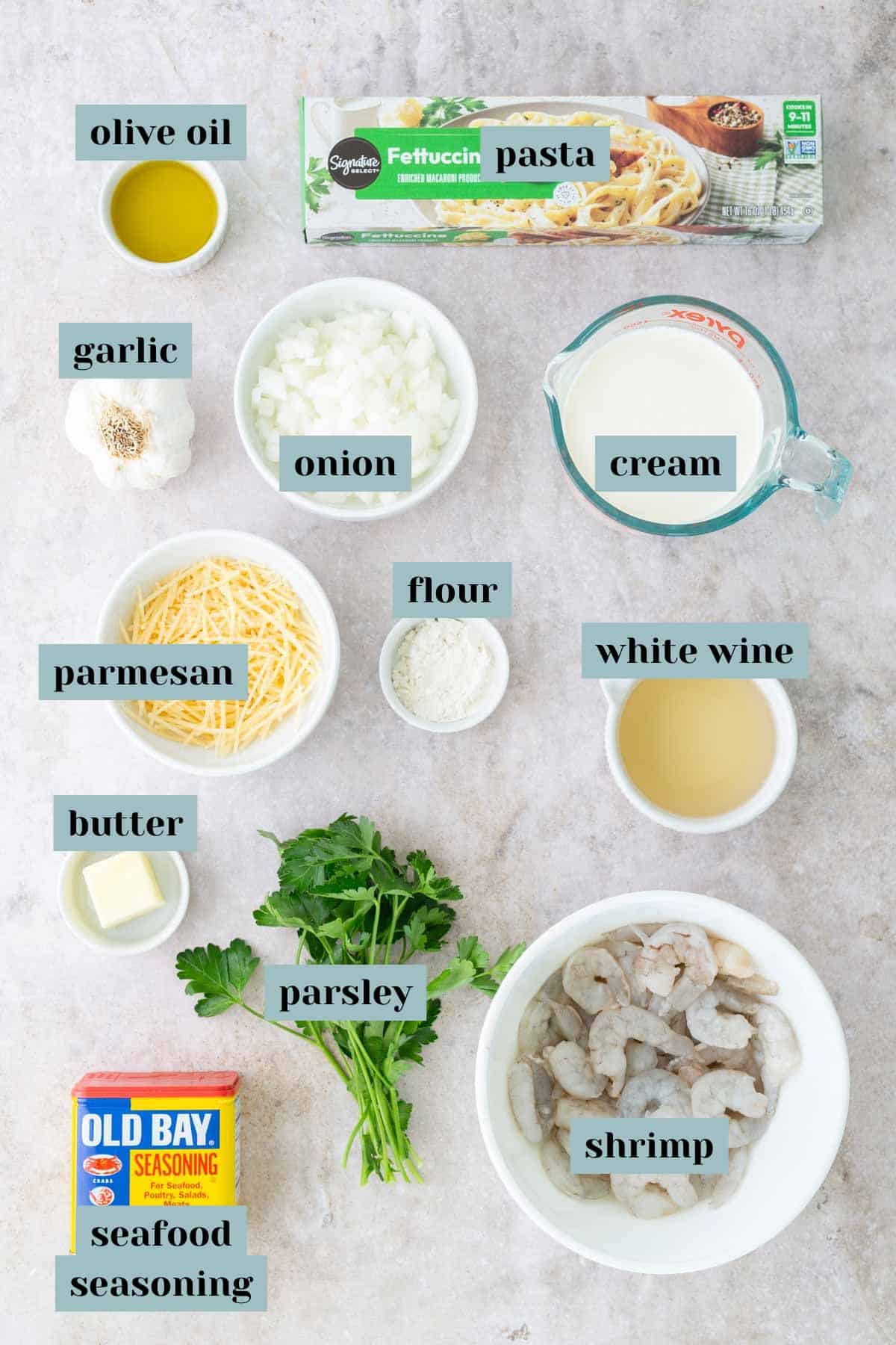 Ingredients for a pasta dish neatly arranged include fettuccine, shrimp, garlic, onion, cream, white wine, parmesan, flour, butter, parsley, olive oil, and seafood seasoning.