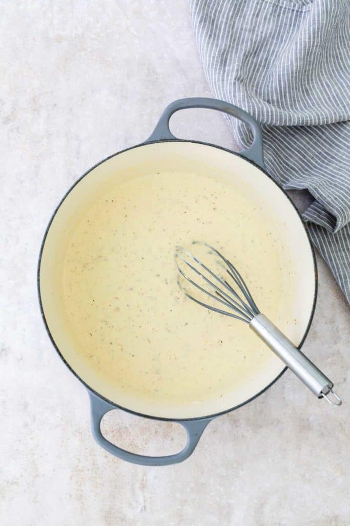 A gray pot with creamy sauce being whisked. Striped cloth beside the pot.