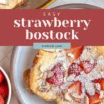 Plate of strawberry bostock topped with powdered sugar and almonds, next to a tray of more bostock and a bowl of fresh strawberries.