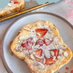 Slice of strawberry bostock with almonds and powdered sugar on a plate.