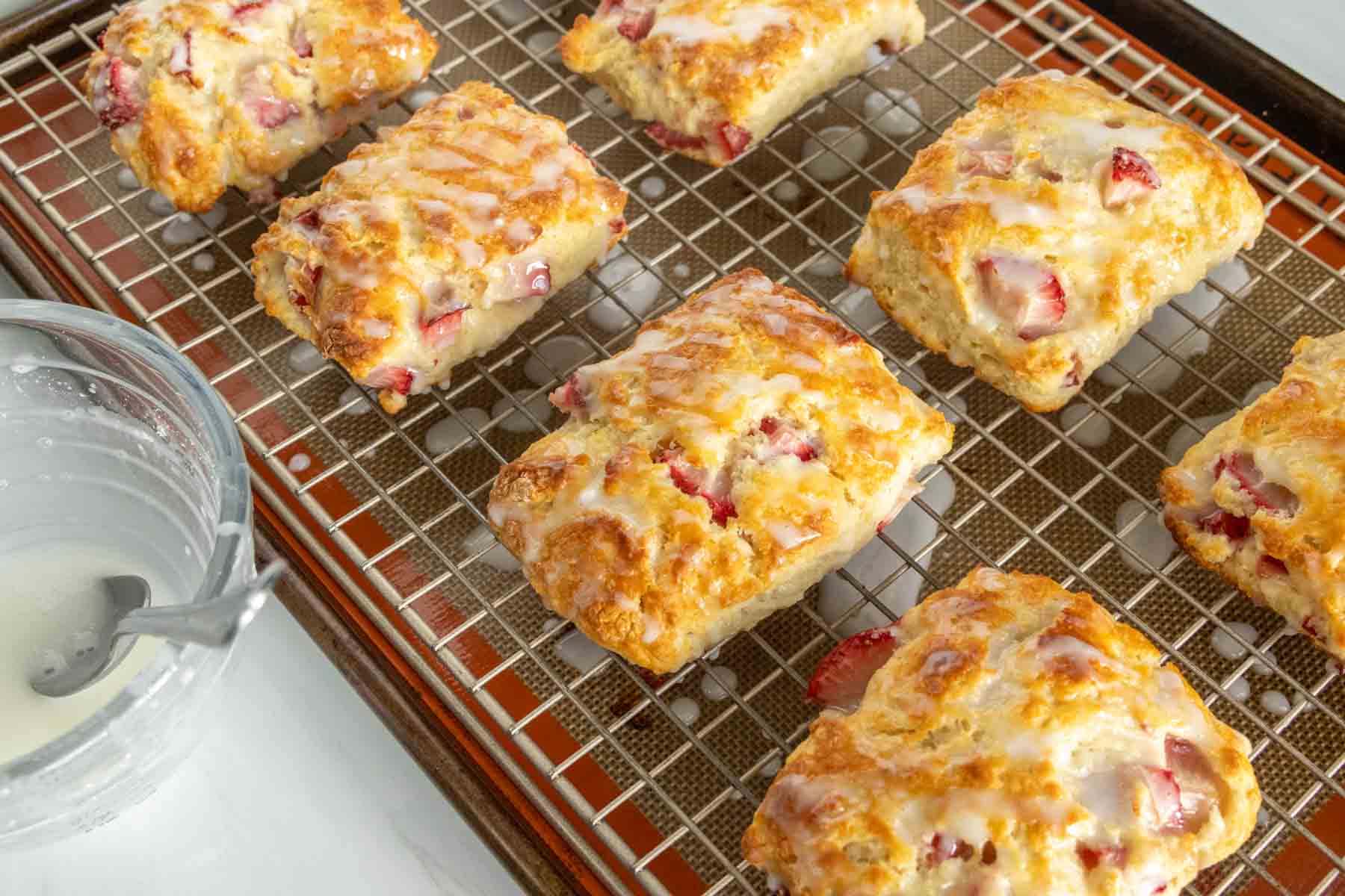 Glazed strawberry biscuits on a wire cooling rack.