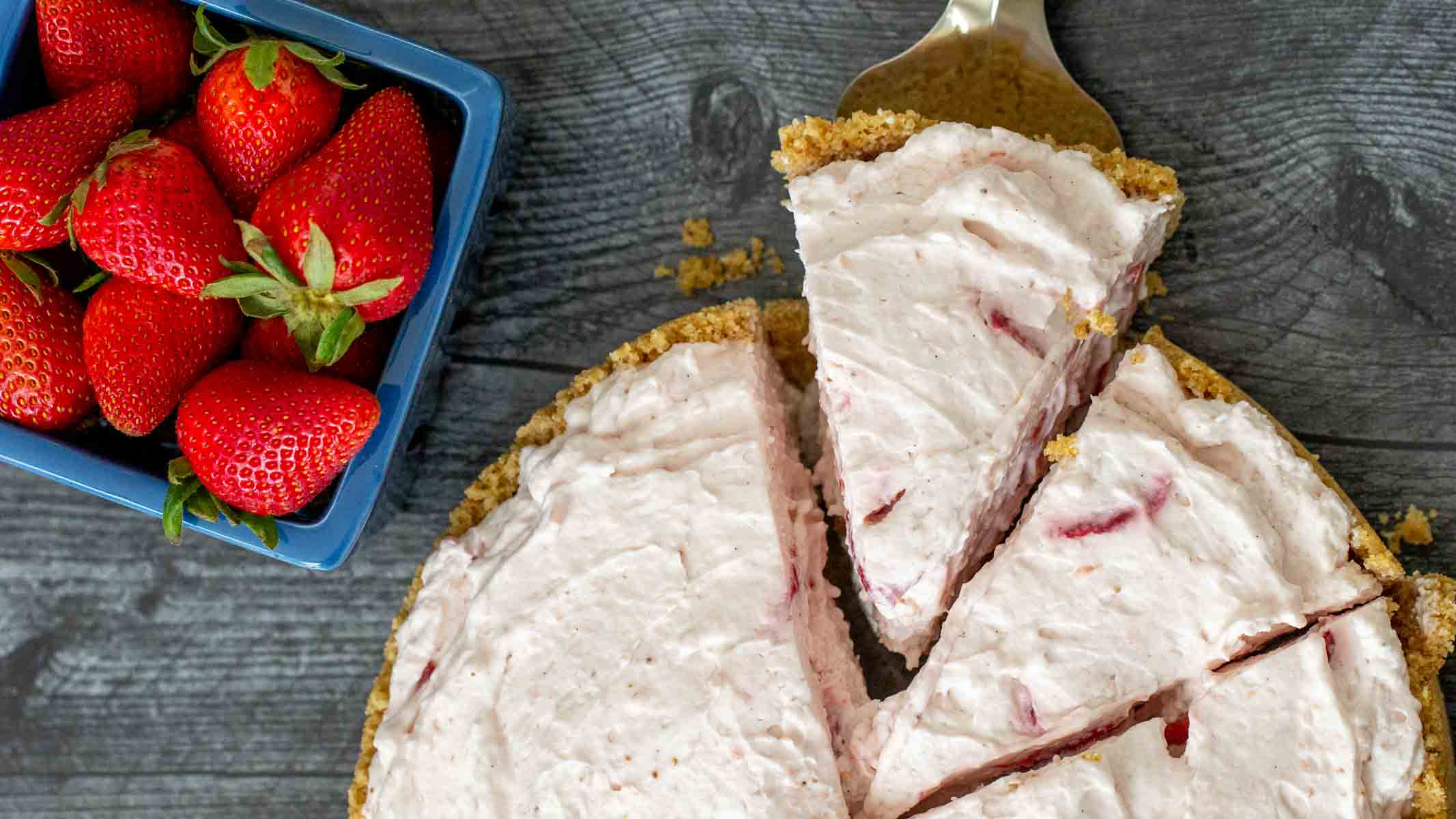 A strawberry chiffon pie being sliced with a box of strawberries next to it.