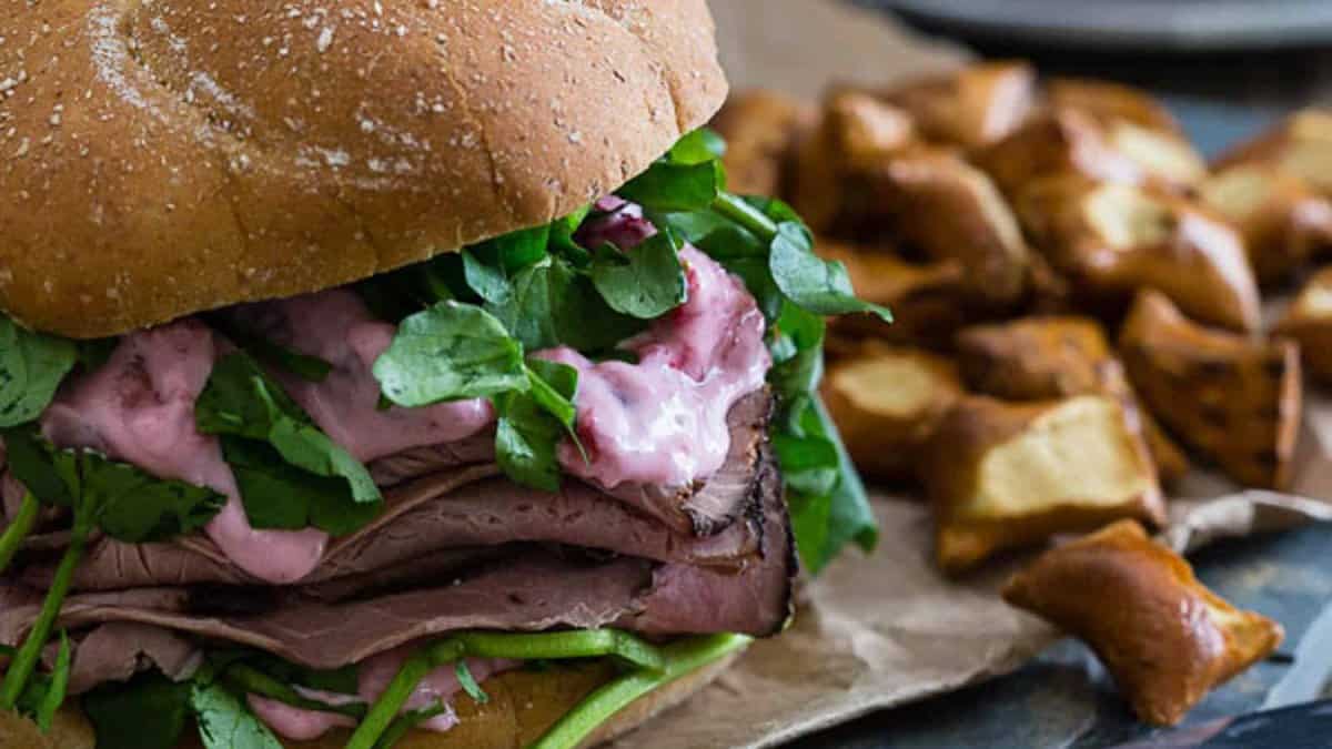 A roast beef sandwich on a plate with strawberry goat cheese sauce.