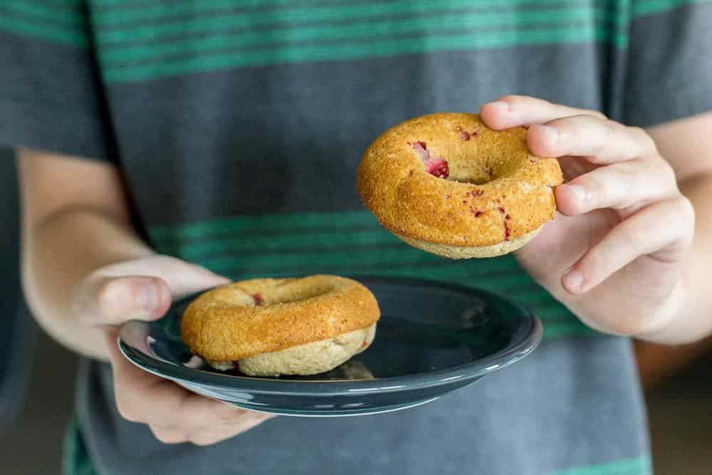 A boy holding a plate with a donut in one hand and a donut in the other hand.